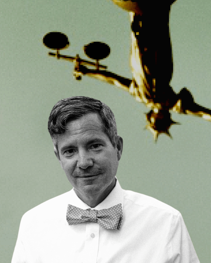 A man in a polka-dot bow tie and white shirt stands in front of a blurred, pixelated background featuring the Statue of Liberty holding an object with two round shapes.